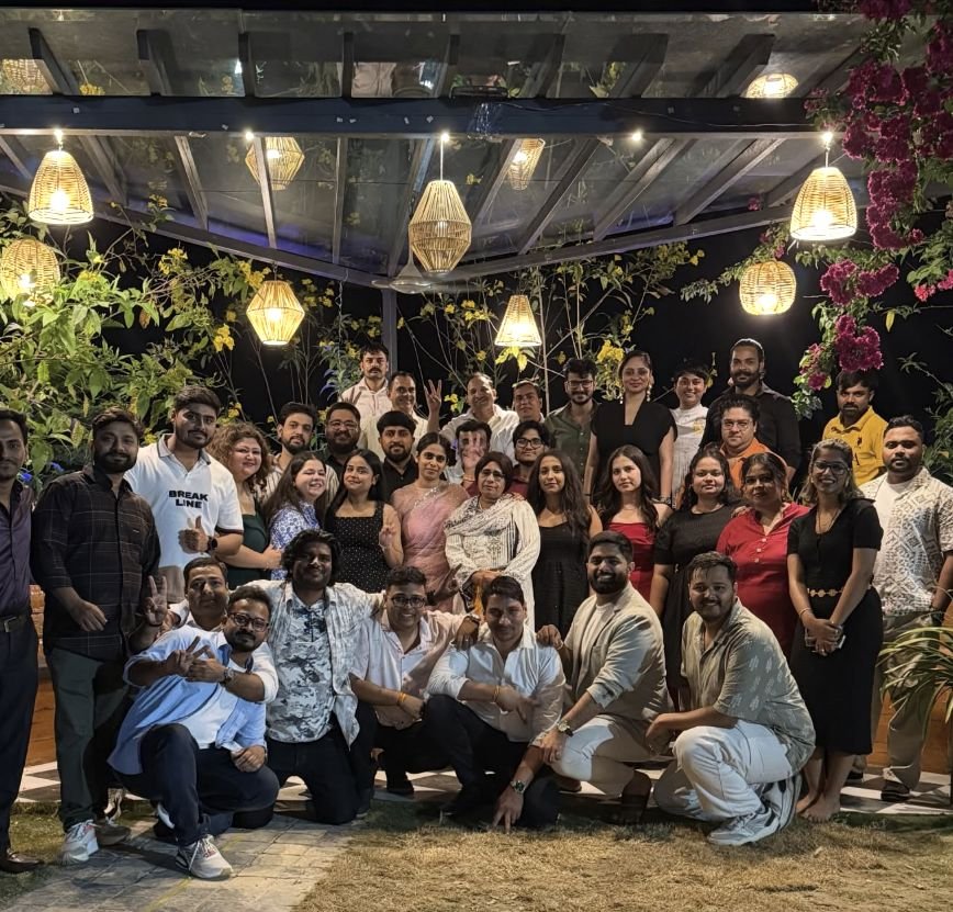 A large group gathered at night under a lantern-lit garden pergola.