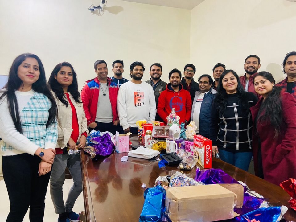 Team gathered around a table full of unwrapped gifts at a year-end gift exchange.